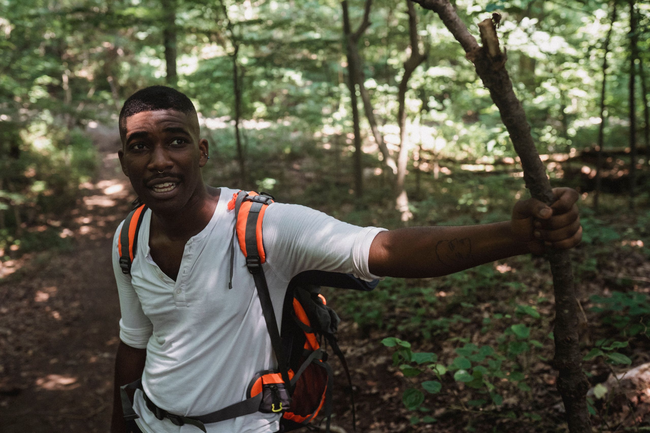 Tired African American man in casual clothes with backpack climbing in green forest in daylight